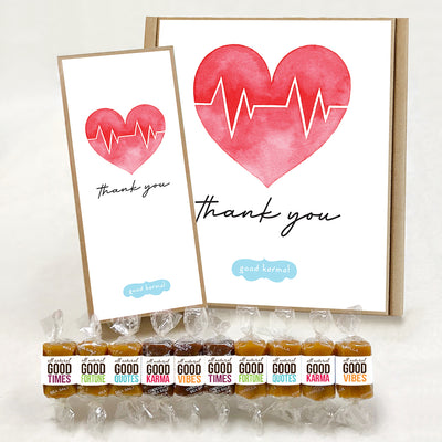Good Karmal caramel gift boxes featuring a sweet illustration of a red heart and medical EKG graph with the words, "Thank you." Caramels shown are wrapped in positive words, Good Times; Good Fortune; Good Quotes; Good Karma; and Good Vibes. Sea salt, Chocolate Sea Salt and Vanilla caramels.