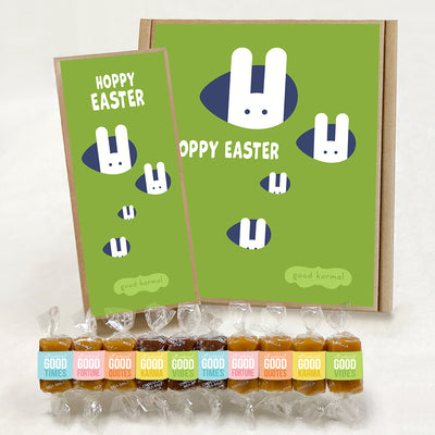 Good Karmal caramel gift boxes that show four white bunnies popping their heads out of egg-shaped rabbit holes and the words "Hoppy Easter." Caramels shown are wrapped in positive words, Good Times; Good Fortune; Good Quotes; Good Karma; and Good Vibes. Sea salt, Chocolate Sea Salt and Vanilla caramels.