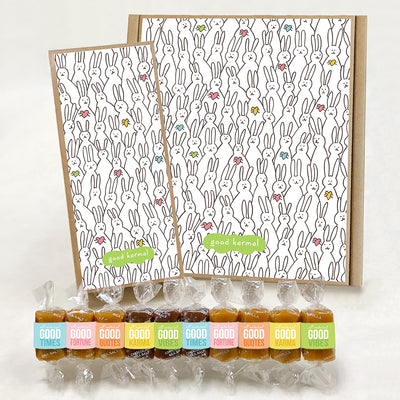 Good Karmal caramel gift boxes covered in illustrated black and white bunnies holding colored hearts. Caramels shown are wrapped in a pastel  palette and the positive words, Good Times; Good Fortune; Good Quotes; Good Karma; and Good Vibes. Sea salt, Chocolate Sea Salt and Vanilla caramels.