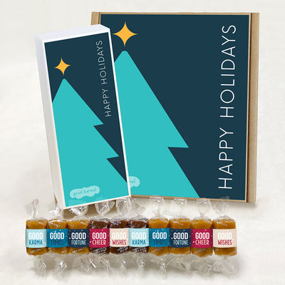 Starlit Holiday caramel gift boxes with blue tree and yellow star topper that says Happy Holidays. Gift box is filled with all-natural caramels wrapped in positive quotes.