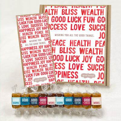 Multi-flavor caramel holiday gift box filled with caramels wrapped in positive quotes and good cheer, good wishes, good fortune, good times and good karma. The outside of the gift box says, "Wishing you all the good things."" and shows graphic design of red words, Health, Bliss, Wealth, Good Luck, Fun, Success, Love and Joy. These are Good Karmal's holiday caramels.
