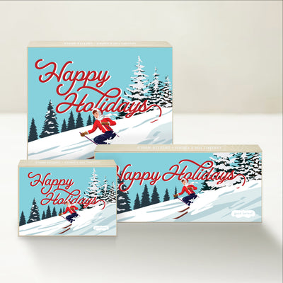 Three Good Karmal caramel gift boxes featuring a skier in a snowy landscape and the words "Happy Holidays."

