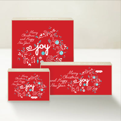 Three holiday-themed Good Karmal caramel gift boxes with messages of Joy, Merry Christmas, and Happy New Year. 