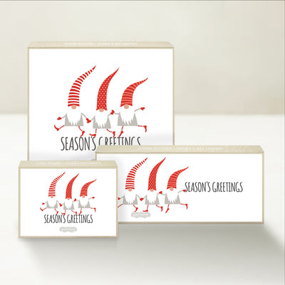 Three holiday-themed Good Karmal caramel gift boxes featuring whimsical gnomes holding hands and wishing season's greetings.