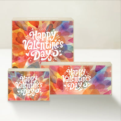 Three Good Karmal caramel gift boxes that say "Happy Valentine's Day" on a background filled with overlapping pastel hearts.