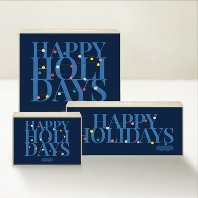 Three holiday-themed Good Karmal caramel gift boxes featuring colorful string lights and happy holiday wishes.