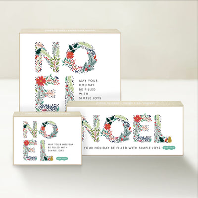 Three holiday-themed Good Karmal caramel gift boxes with a whimsically illustrated Noel and wishes for holidays filled with simple joys.