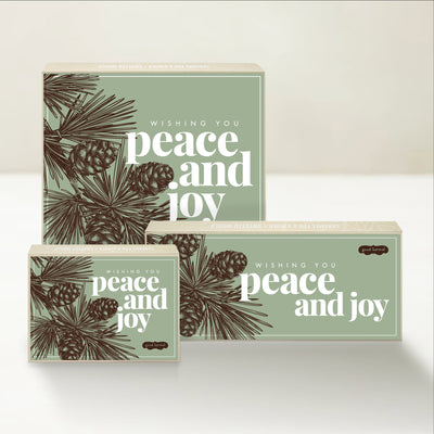 Three holiday-themed Good Karmal caramel gift boxes with an illustration of pinecones and the words "wishing you peace and joy."